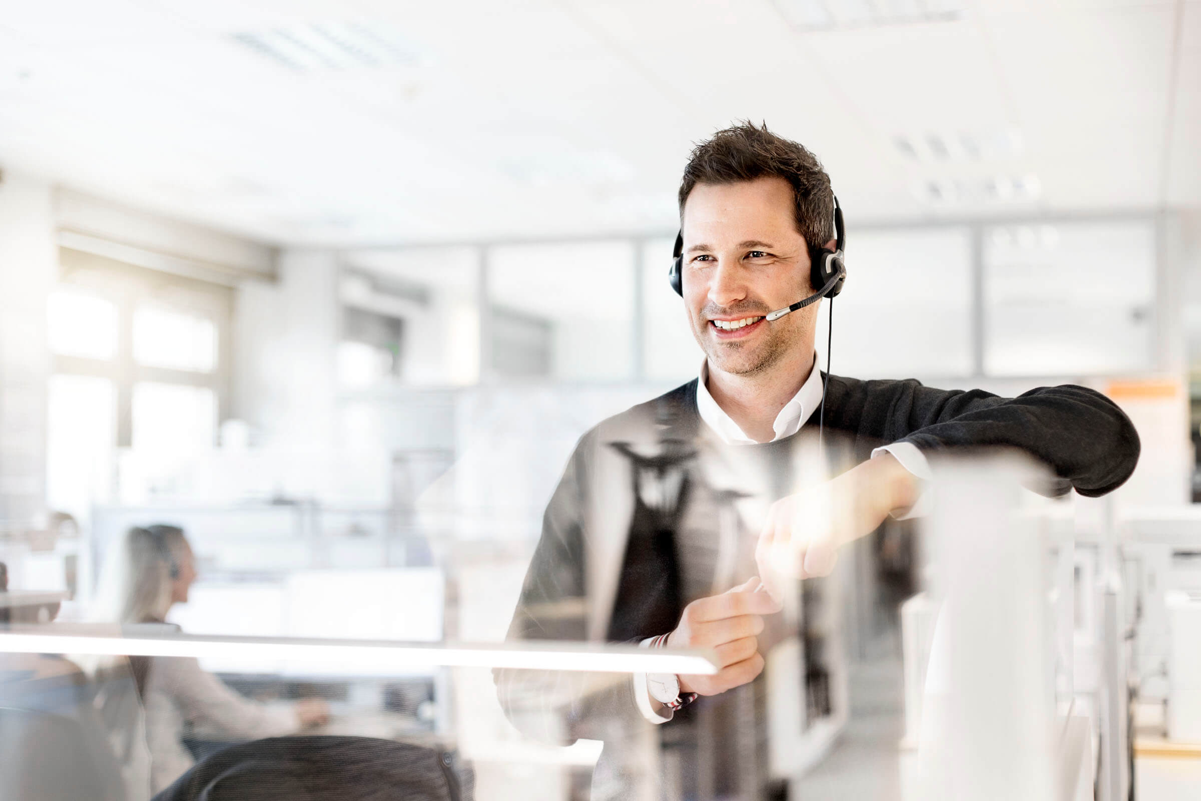 Ein Business Partners Mitarbeiter führt im Büro ein Kundengespräch über sein Headset. Ein Business Partners Mitarbeiter führt im Büro ein Kundengespräch über sein Headset.