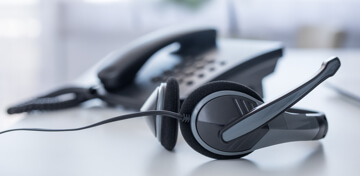 Ein Headset liegt neben einem modernen Tischtelefon auf einer hellgrauen Schreibtischfläche.