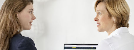Zwei Frauen unterhalten sich lebhaft vor einem geöffneten Laptop-Bildschirm. Darauf ist die comdirect Webseite zu sehen.
