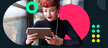Eine rothaarige, junge Frau mit Ponyfrisur sitzt in einem Caf&eacute; und schaut auf ihr wei&szlig;es Tablet. Sie liest den comdirect Newsletter.