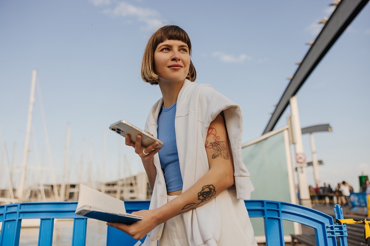 Eine Frau sitzt an einem Hafen mit ihrem Handy in der Hand.