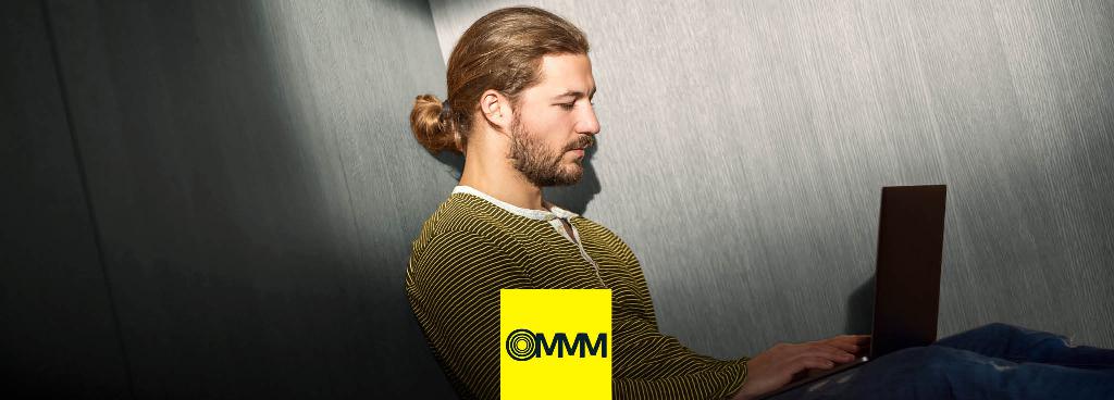 Ein junger Mann sitzt auf dem Boden mit einem Laptop auf seinen Knien.