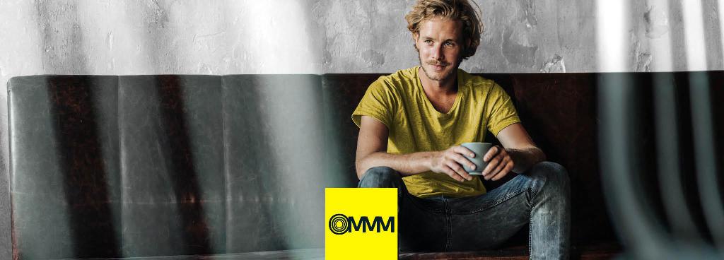 Ein junger Mann mit Schnurrbart und gelbem Shirt sitzt auf einem Sofa.