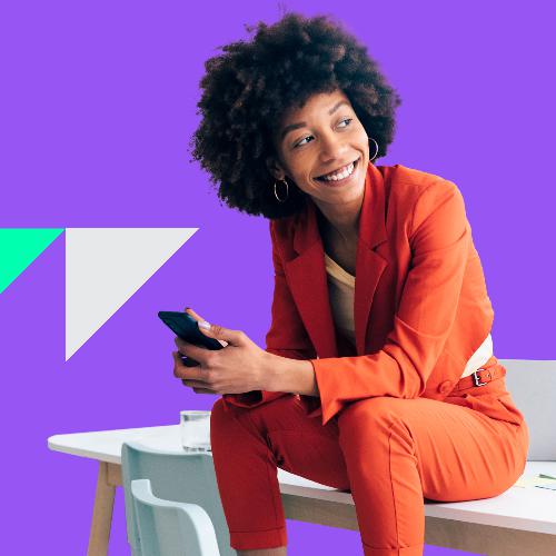 Eine junge Frau in einem Anzug sitzt lächelnd auf einem Tisch.