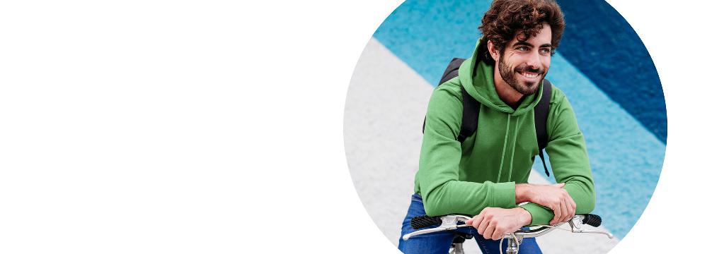 Ein junger Mann mit grünem Pulli sitzt auf einem Fahrrad und hat die Arme auf den Lenker gelegt. Er schaut nach oben und lächelt über die guten Dispositionskredit Konditionen.