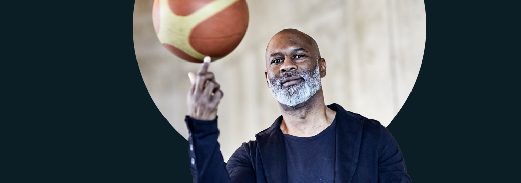 Ein bärtiger Mann balanciert einen Basketball auf seinem Zeigefinger.