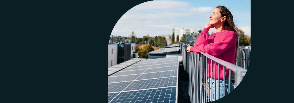 Eine Frau steht entspannt auf einem Balkon neben Solarpaneelen in der Sonne.
