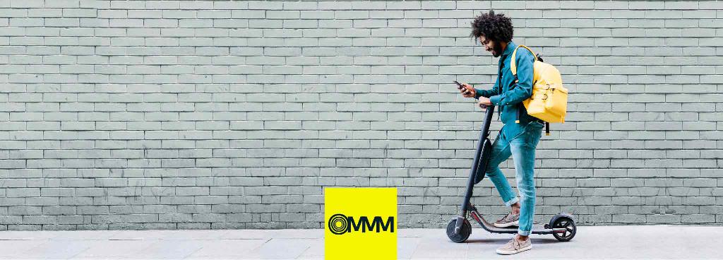 Ein junger, lockiger Mann steht entspannt mit einem Fuß auf einem Elektroroller.