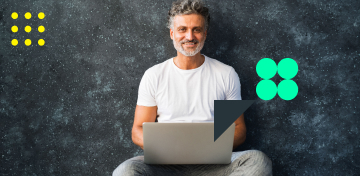 Ein lächelnder Mann mit grauen Haaren und Bart sitzt vor einer dunklen Wand.