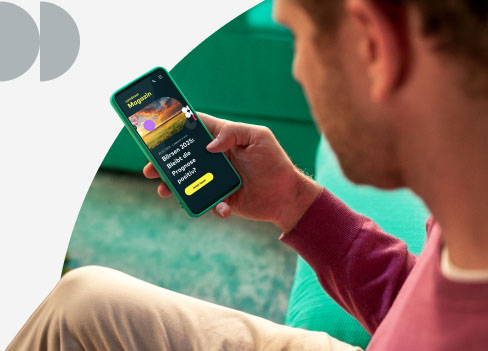 Auf dem Sofa sitzt ein Mann, der auf sein Smartphone schaut. Im Hintergrund ist ein Teppich zu erkennen.