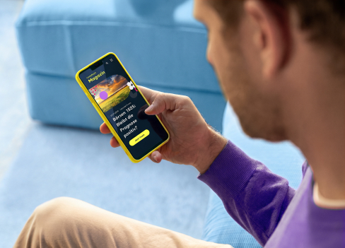 Auf dem Sofa sitzt ein Mann, der auf sein Smartphone schaut.