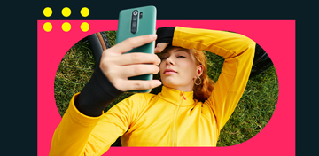Eine junge Frau liegt im Gras und schaut auf das kostenlose Tagesgeld Plus Konto in der comdirect App auf ihrem Handy.