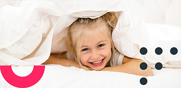 Ein blondes Mädchen lugt unter einer weißen Bettdecke hervor. Es stützt den Kopf auf die Arme und lächelt. Es befindet sich ein Störer auf dem Bild mit dem Text „Bis 31.01.“