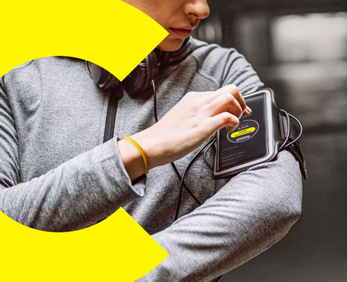 Eine Frau in Joggingkleidung trägt ihr Smartphone am Arm. Sie kauft eine Aktie über den Soforthandel.