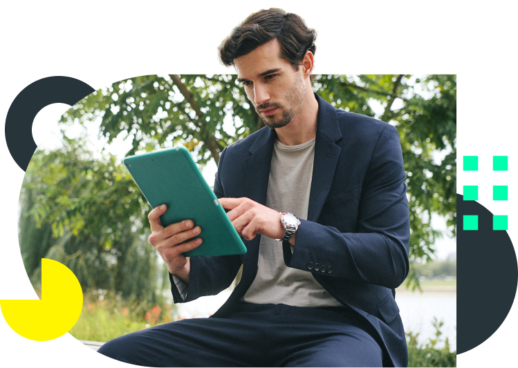 Ein junger Mann sitzt entspannt im Grünen und liest auf seinem Tablet das comdirect Magazin.