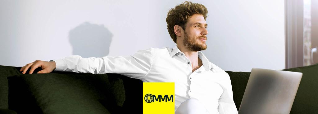 Ein Mann sitzt mit seinem PC auf einem Sofa und schaut entspannt in die Ferne.