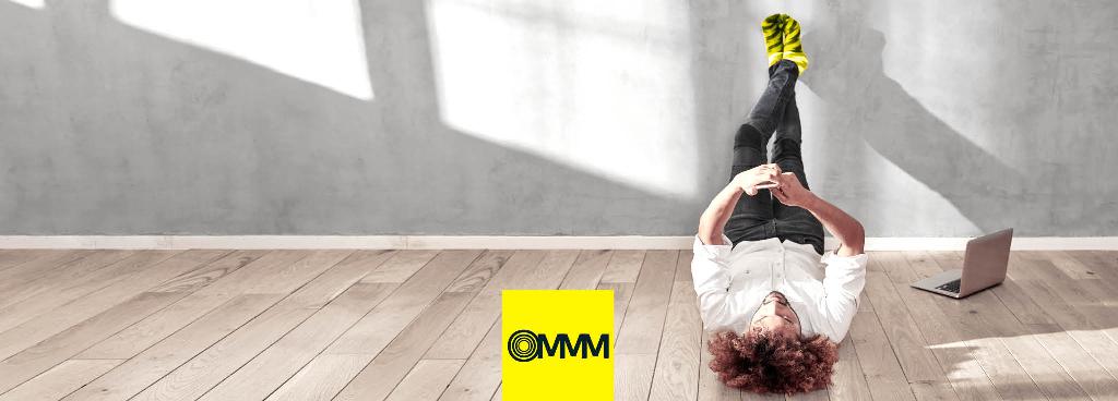 Ein junger Mann liegt entspannt auf dem Fußboden und guckt auf sein Handy.