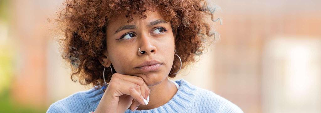 Eine junge Frau mit lockigen Haaren blickt nachdenklich nach oben.