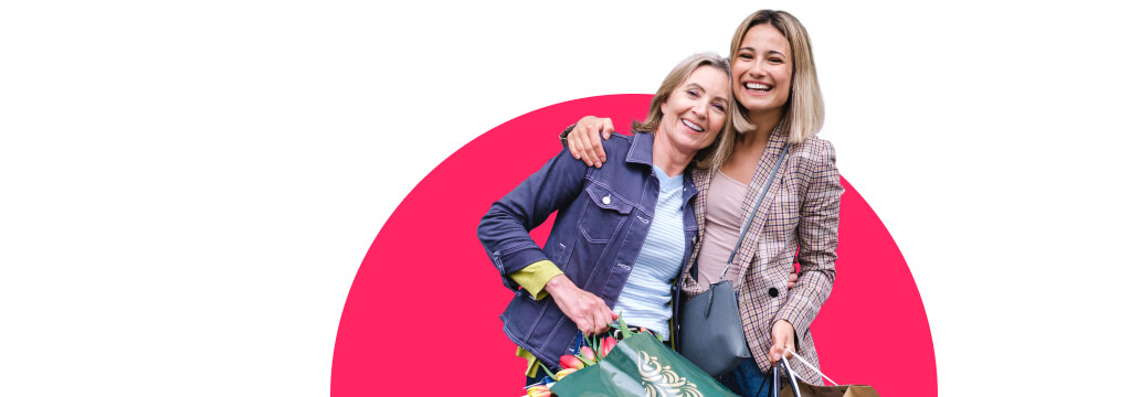 Zwei lachende Frauen umarmen sich. Sie haben volle Einkaufstaschen in den Händen. Mit dem Visa 3-Raten-Service shoppen sie clever. 