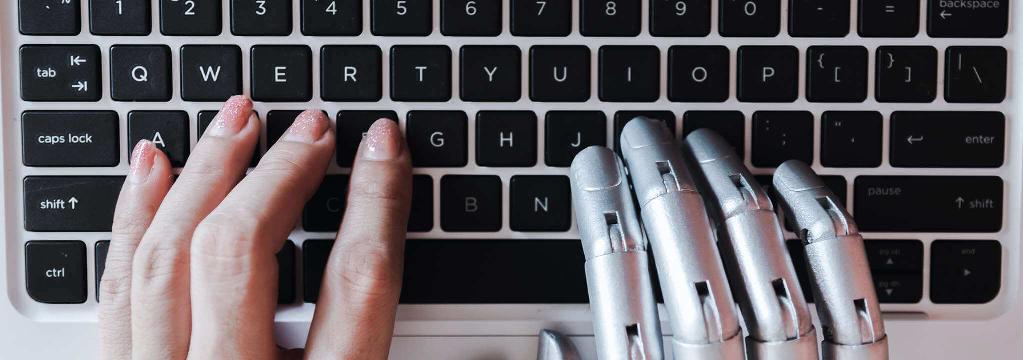 Eine Frauen- und eine Roboterhand tippen auf einer Tastatur.