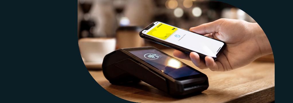 Smartphone-Display mit comdirect Visa-Debitkarte schwebt &uuml;ber Bezahlterminal.