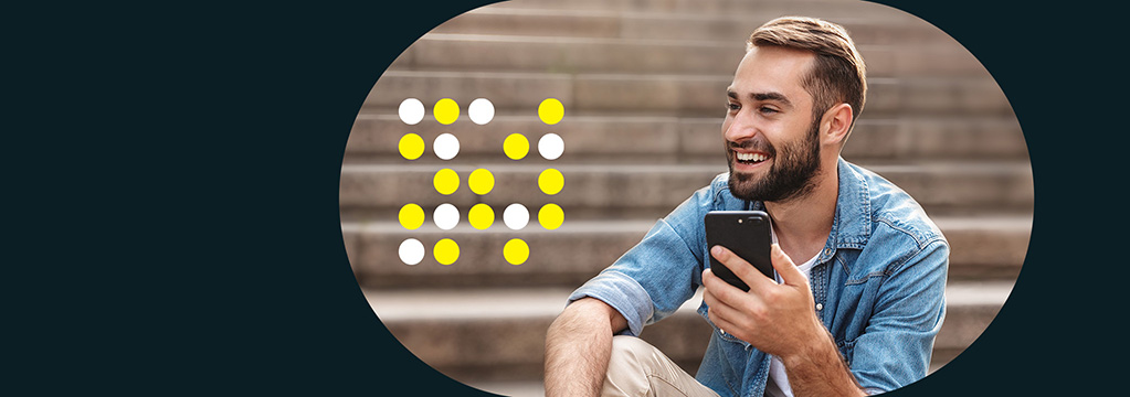 Ein junger Mann mit Bart sitzt auf einer Steintreppe und hält sein Handy in der Hand.