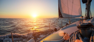 Auf einem Segelschiff sieht man einen Sonnenuntergang im Meer.