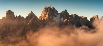 Eine felsige Bergkette wird oberhalb einer Nebelwolke von der Sonne beschienen.