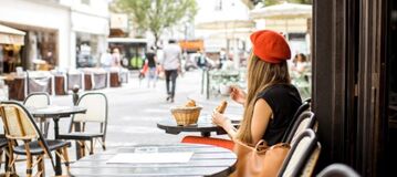 Eine Frau mit roter M&uuml;tze sitzt an einem Cafe-Tisch.