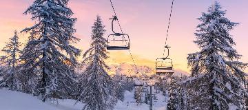 Zwei Skilift-Gondeln gleiten an schneebedeckten B&auml;umen vorbei.