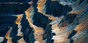 Die Terrassen einer Tagebau-Mine leuchten schwarz-gelb-orange in der Sonne.