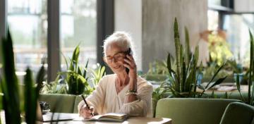 Eine Frau sitzt telefonierend in einem Café und macht sich Notizen.