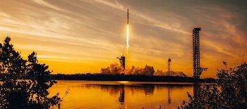 Eine Rakete hebt vor einem orangefarbenen Himmel von einer Abschussrampe ab.