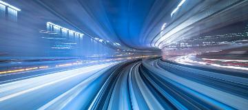 Auf einer mehrspurigen Straße rasen Autos als farbige Lichtpunkte durch die Nacht.
