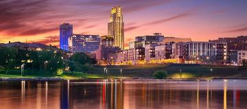 In der Abendsonne ist eine Skyline zu sehen, die sich in einem See spiegelt.