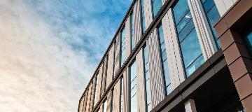 Wei&szlig;e Wolken spiegeln sich in einer modernen Glas- und Holzfassade.