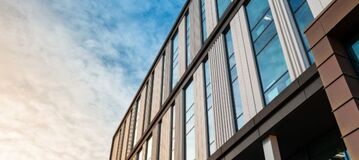 Wei&szlig;e Wolken spiegeln sich in einer modernen Glas- und Holzfassade.