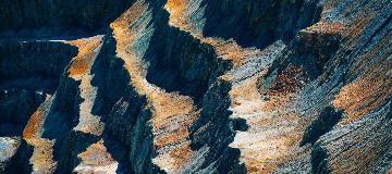 Die Terrassen einer Tagebau-Mine leuchten schwarz-gelb-orange in der Sonne.