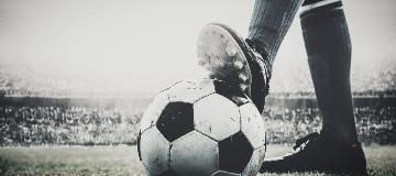 Ein Stollen-Schuh tritt in einem Stadion gegen einen Fu&szlig;ball.