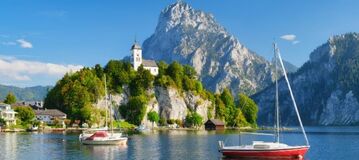 Ein Bergsee mit zwei Segelbooten und einer Kirche, die auf einer felsigen Anh&ouml;he steht.