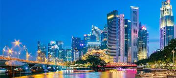 Die Skyline des Finanzdistrikts von Singapur spiegelt sich farbig im Wasser.