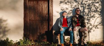 Zwei M&auml;nner sitzen nebeneinander auf einer Bank in der Sonne.
