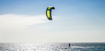 Ein Kitesurfer surft im Meer vor blauem Himmel.