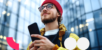 Ein junger Mann schaut glücklich von seinem Smartphone auf in Richtung Himmel.