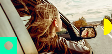 Eine Frau hält ihren Kopf und den rechten Arm aus dem Fenster eines Autos.