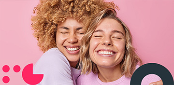 Zwei junge Frauen umarmen sich fest und lachen mit geschlossenen Augen in die Kamera.