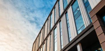 Wei&szlig;e Wolken spiegeln sich in einer modernen Glas- und Holzfassade.