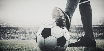 Ein Stollen-Schuh tritt in einem Stadion gegen einen Fu&szlig;ball.