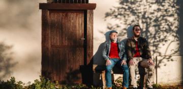Zwei M&auml;nner sitzen nebeneinander auf einer Bank in der Sonne.