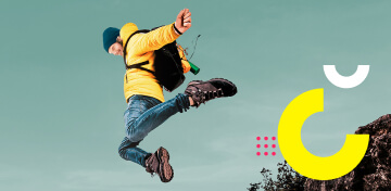 Ein Mann mit gelber Jacke und Bergwanderschuhen springt in die Luft.